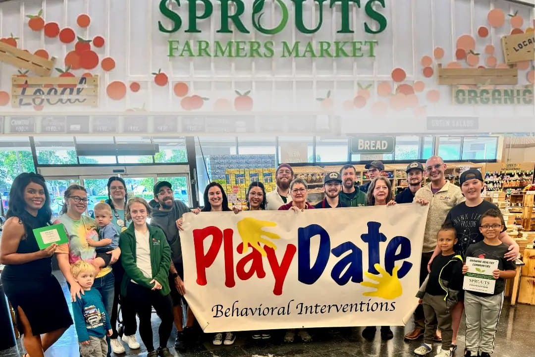 PlayDate staff, families and children holding a PlayDate Behavioral Interventions banner inside a Sprouts Farmers Market