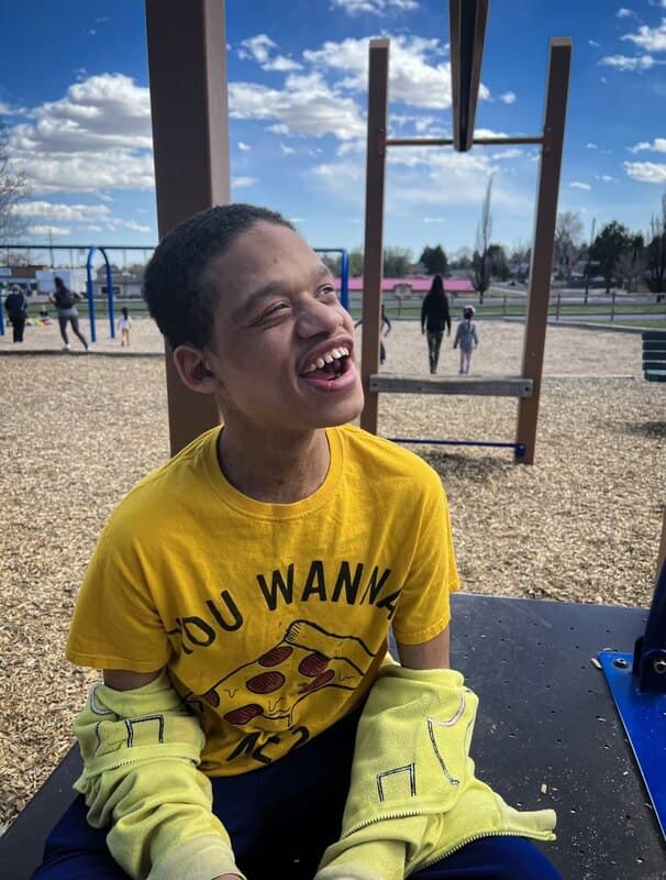 A teenager in a yellow shirt laughing on a playground on a sunny day